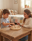 A young boy and girl sitting at a rustic wooden table playing with a wooden peg board game in a warm, cozy child's bedroom.