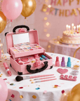 A pink makeup case filled with cosmetics and surrounded by party decorations, including balloons, confetti, a birthday cake, and a 'Happy Birthday' banner, on a white tablecloth.
