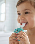 A young child smiling while using a turquoise and white oral irrigator with a cartoon face in a bright bathroom setting.