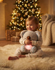 A baby sitting on a fluffy cream rug in a cozy living room, hugging a plush koala toy that glows with a warm pink light. The baby is wearing light-colored pajamas with small dark star patterns.