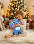 A toddler in cream pajamas sits on a white fluffy rug in a cozy living room, hugging a blue Stitch plush toy in front of a decorated Christmas tree and wrapped gifts.