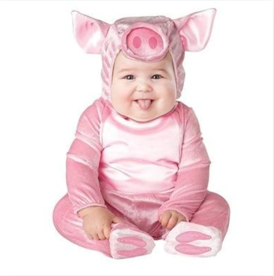 A baby wearing a pink pig costume, sitting and sticking out their tongue against a plain white background.