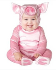 A baby wearing a pink pig costume, sitting and sticking out their tongue against a plain white background.