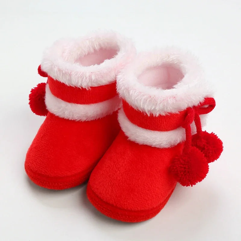 Red baby booties with white fur trim and pom-poms on a light gray background