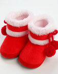 Red baby booties with white fur trim and pom-poms on a light gray background