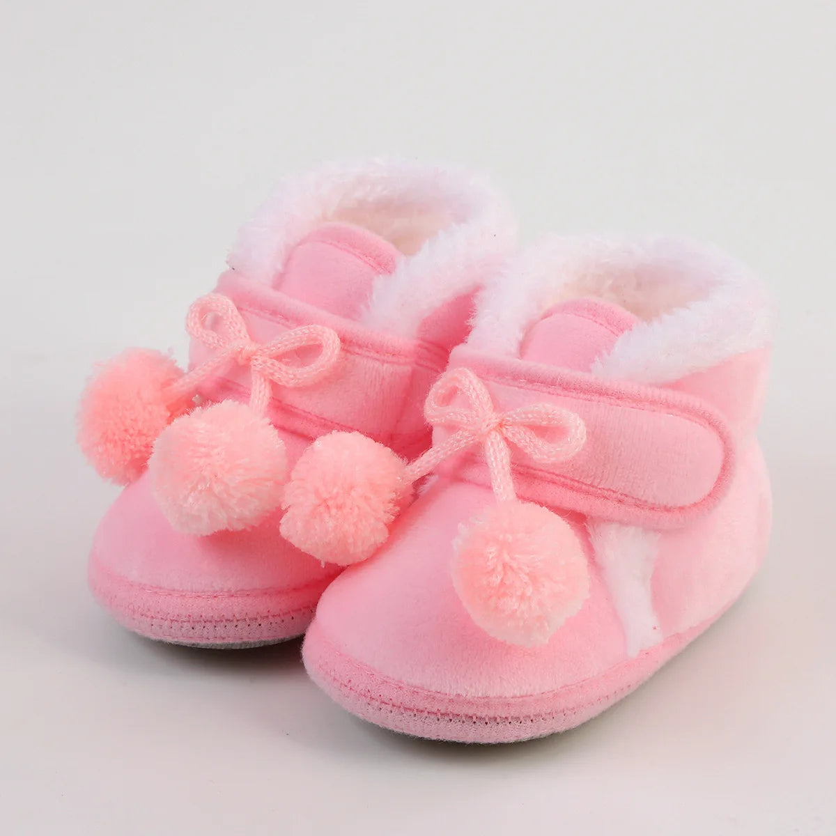Pink baby shoes with bows and pom-poms on a light gray background