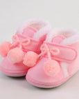 Pink baby shoes with bows and pom-poms on a light gray background