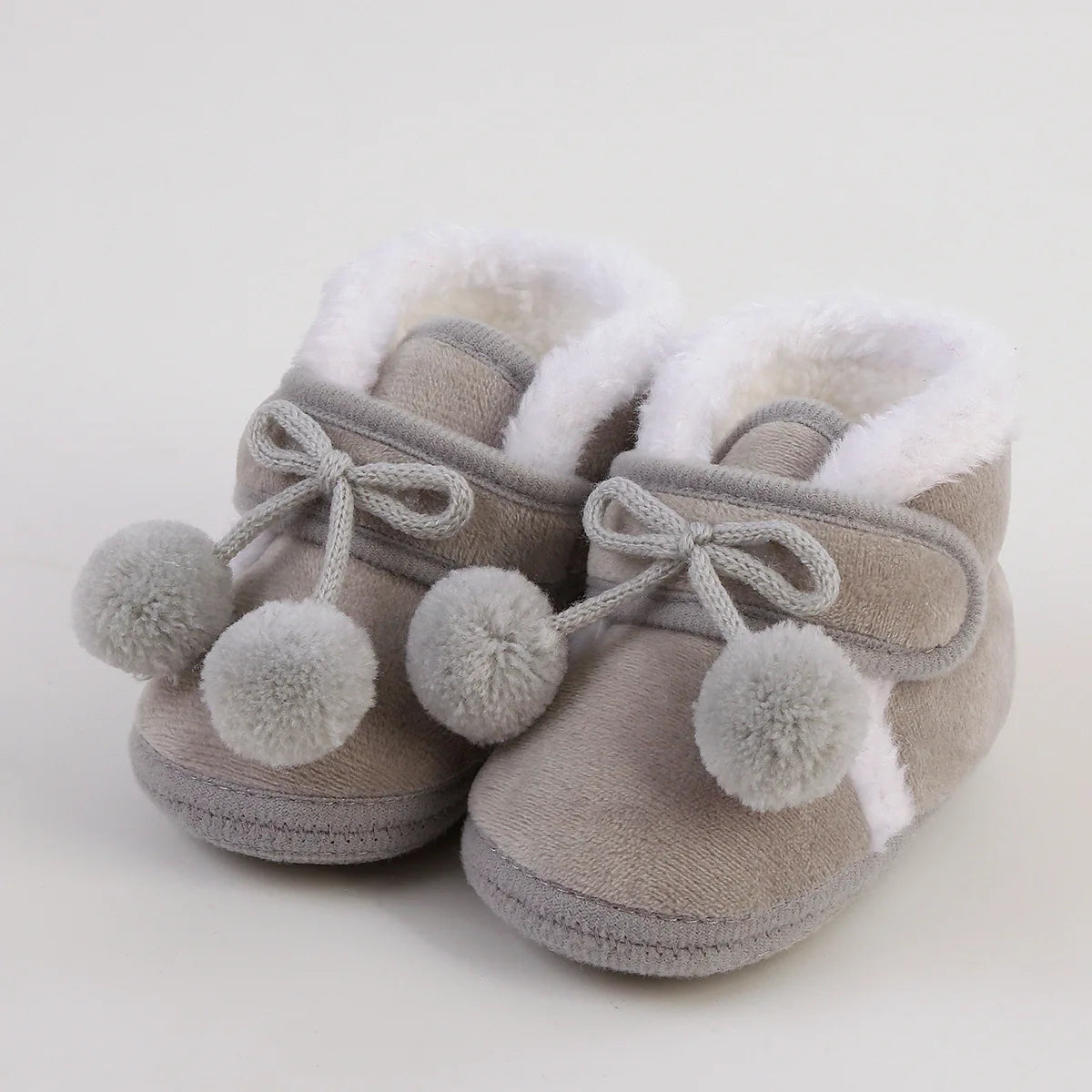 Pair of gray baby shoes with white fur lining and pom-pom details on a light background