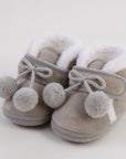 Pair of gray baby shoes with white fur lining and pom-pom details on a light background
