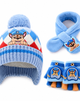 A Paw Patrol-themed baby winter hat, scarf, and mittens set on a white background. The light blue knit hat features a fluffy pom-pom, a red and white argyle pattern, and a cartoon puppy graphic.